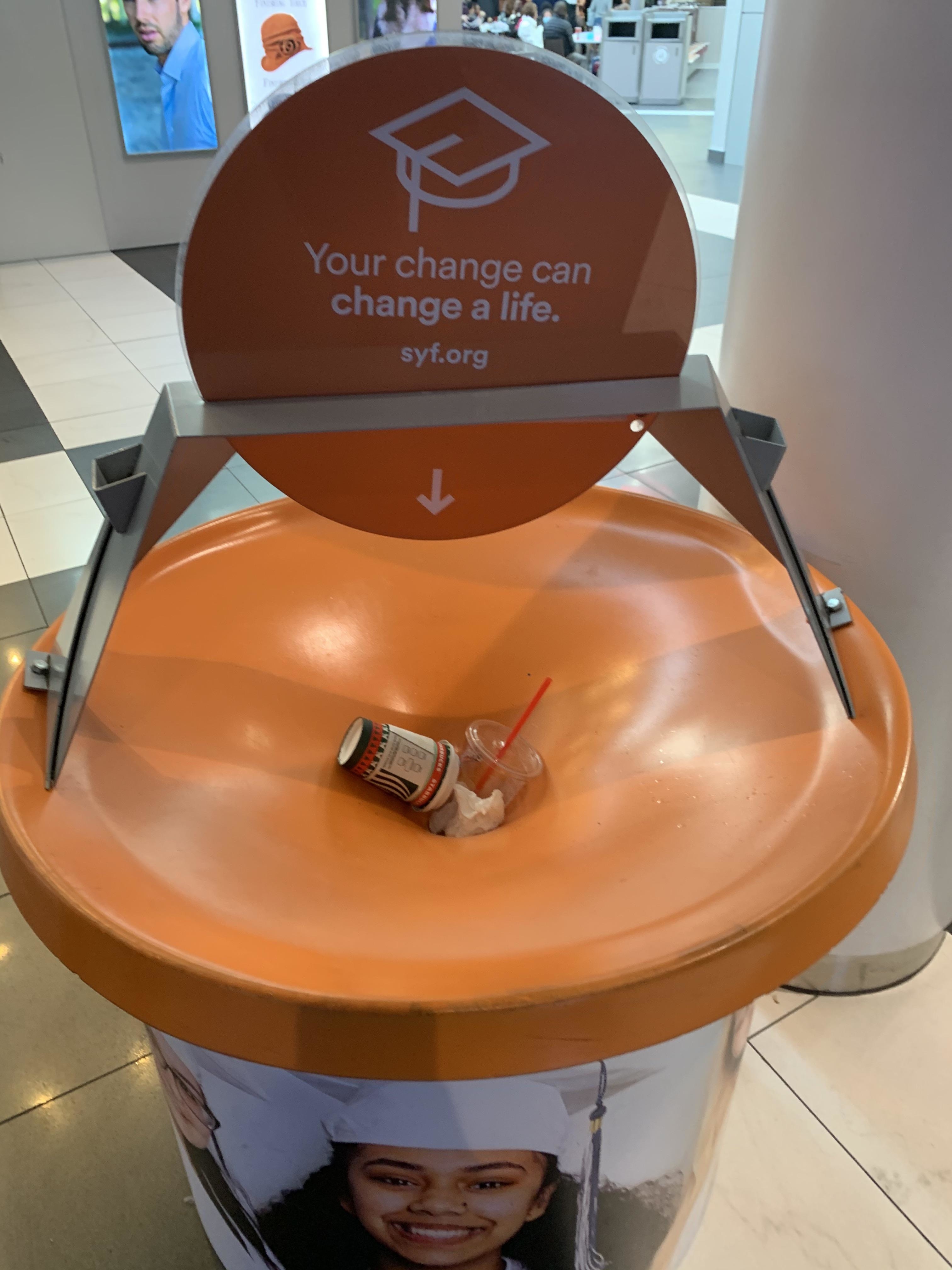Donation station with a sign &quot;Your change can change a life&quot; with trash like a can, plastic cup, and straw on the collection surface
