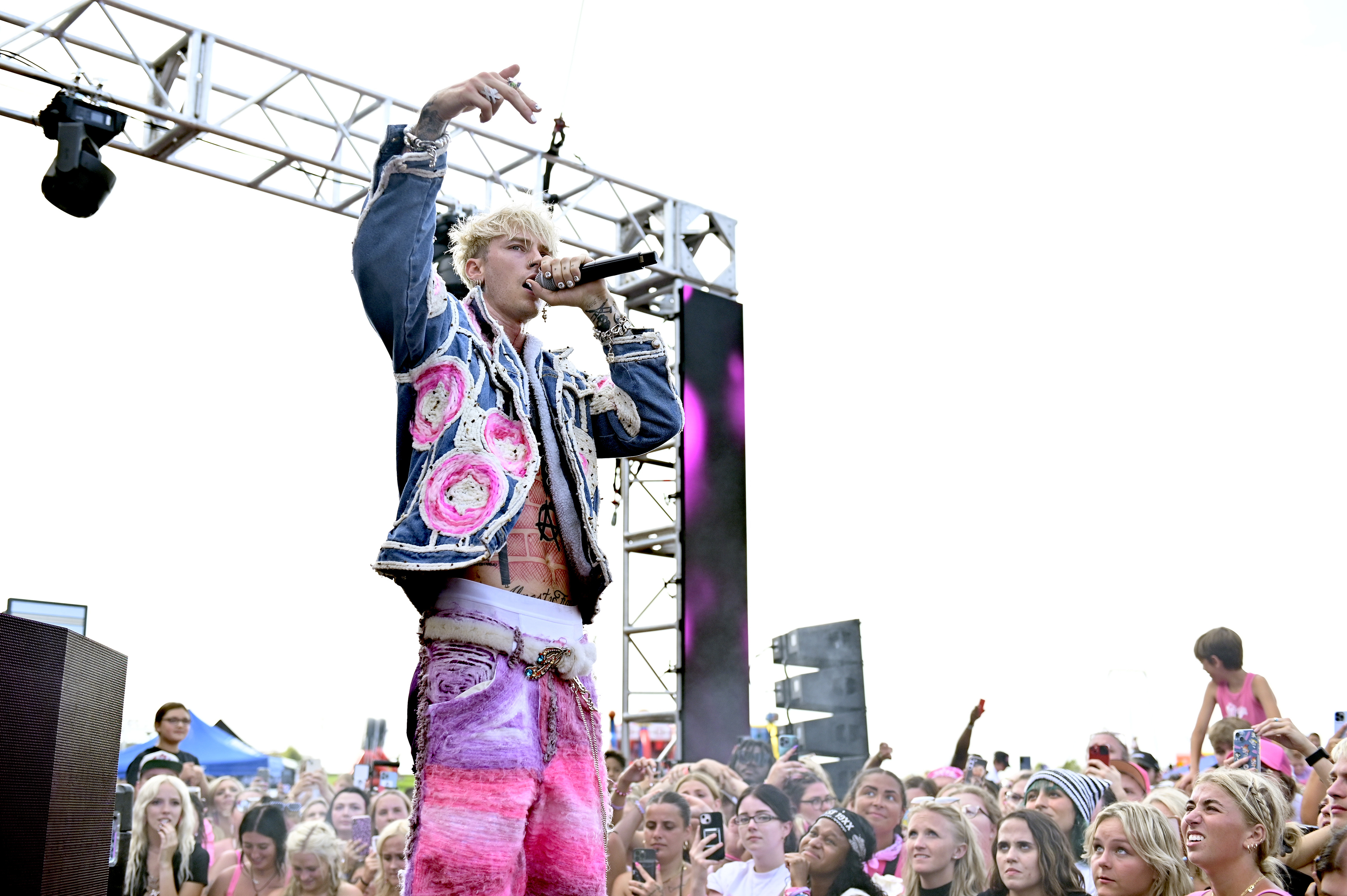 Machine Gun Kelly in a vibrant jacket and pants singing into a microphone on stage before an audience