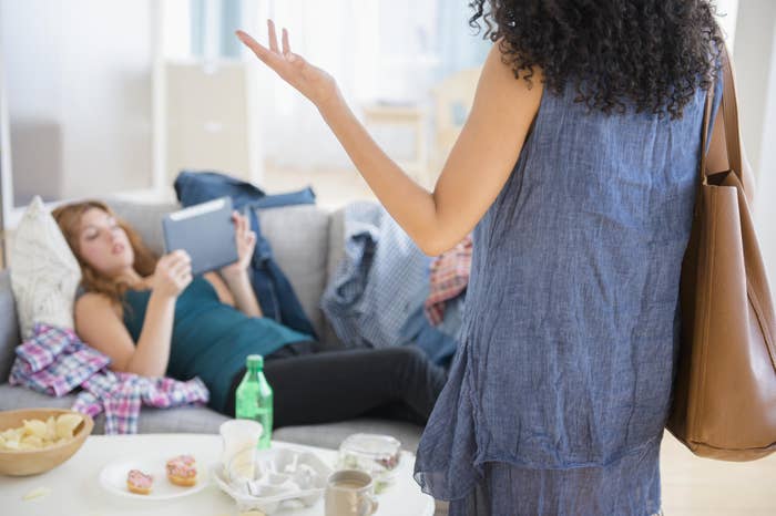 Woman gesturing while talking to a friend lounging on a sofa in a living room with snacks