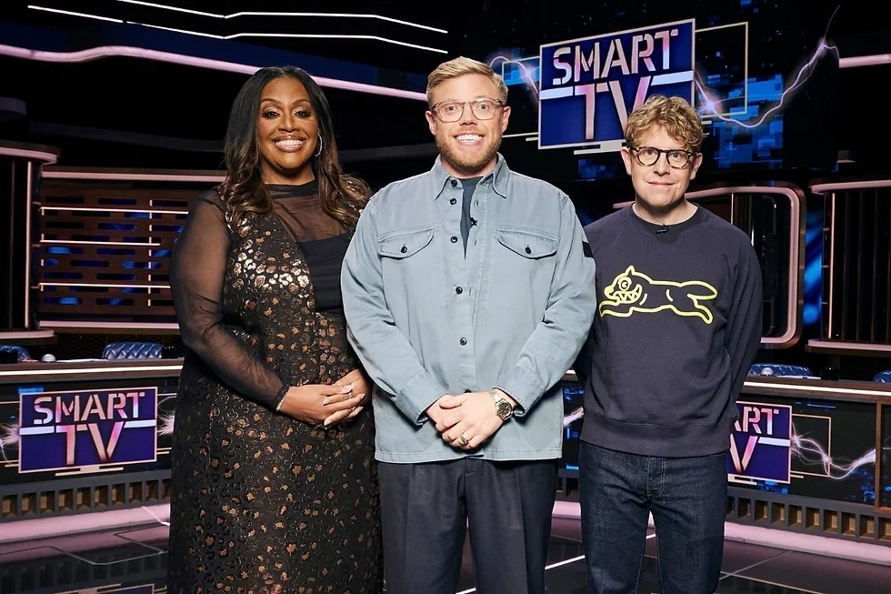Three hosts stand on the set of a TV show titled &#x27;Smart TV,&#x27; smiling for the photo