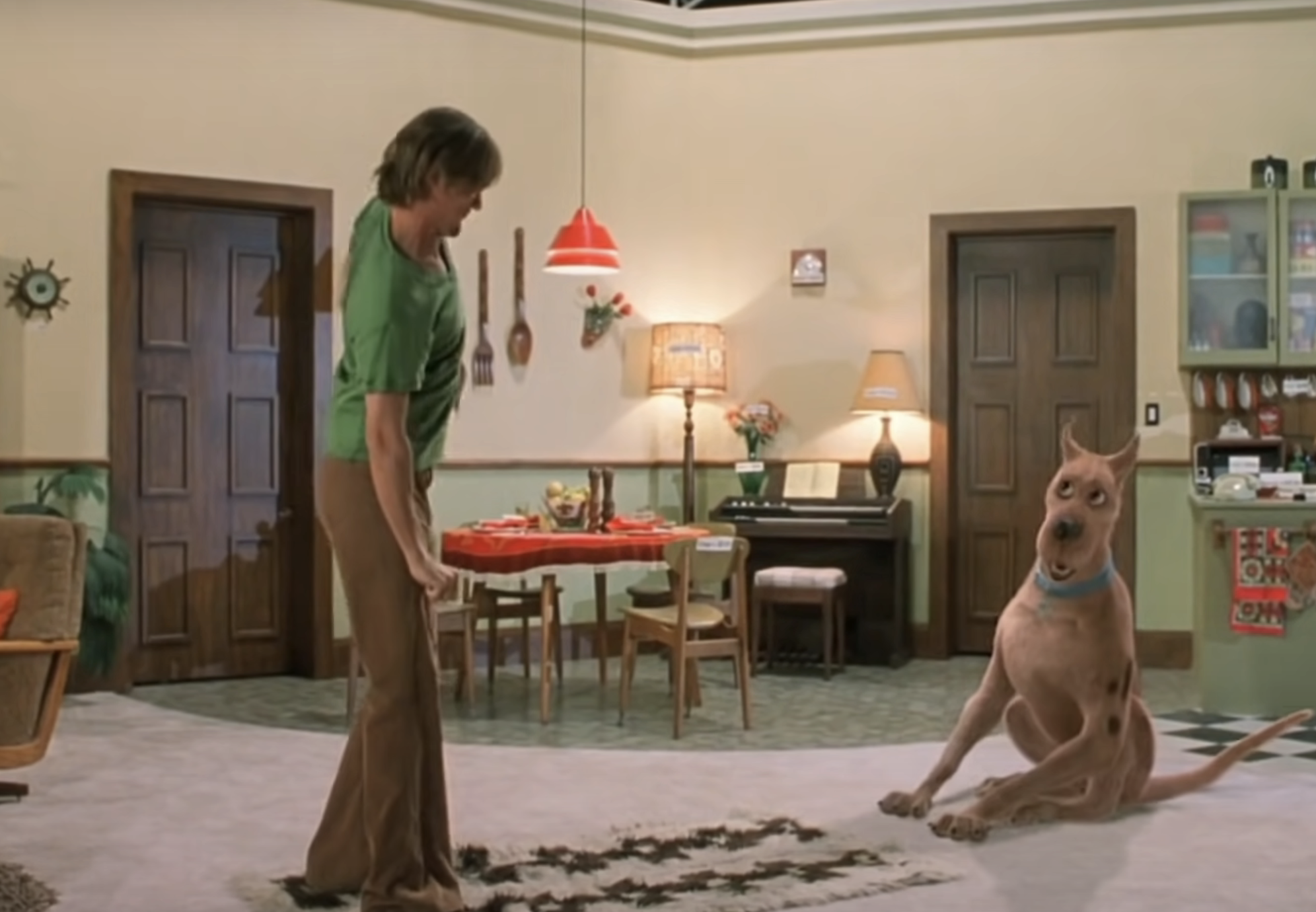 Shaggy, wearing a green tee, stands opposite Scooby-Doo in a room from the movie. Scooby looks guilty