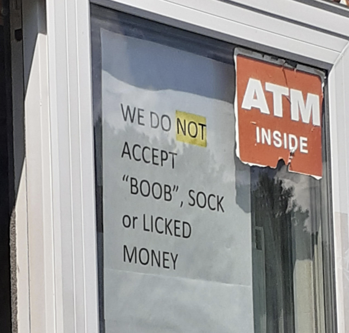 Sign on a window reads &quot;WE DO NOT ACCEPT &#x27;BOOB&#x27;, SOCK OR LICKED MONEY&quot; next to an &quot;ATM inside&quot; sign