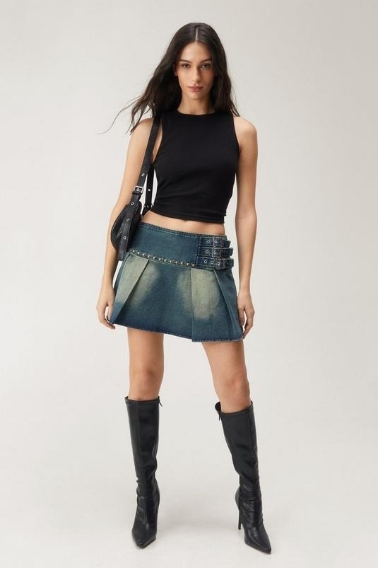 Woman in a black tank top, denim mini skirt, knee-high boots, and carrying a shoulder bag
