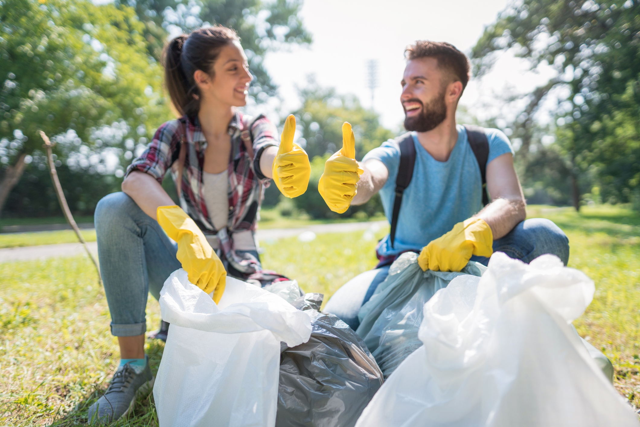 Man and woman giving thumbs-ups while sitting with trash bags, participating in a park cleanup