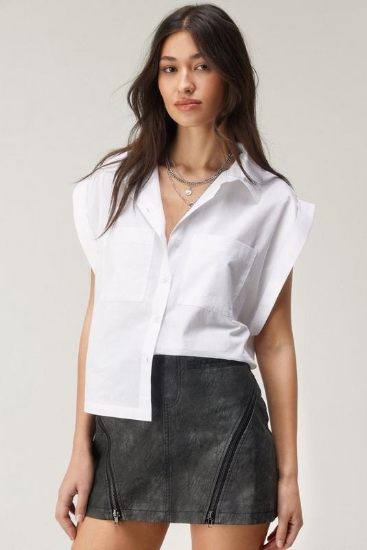 Model wearing a white short-sleeve button-up shirt and black leather miniskirt