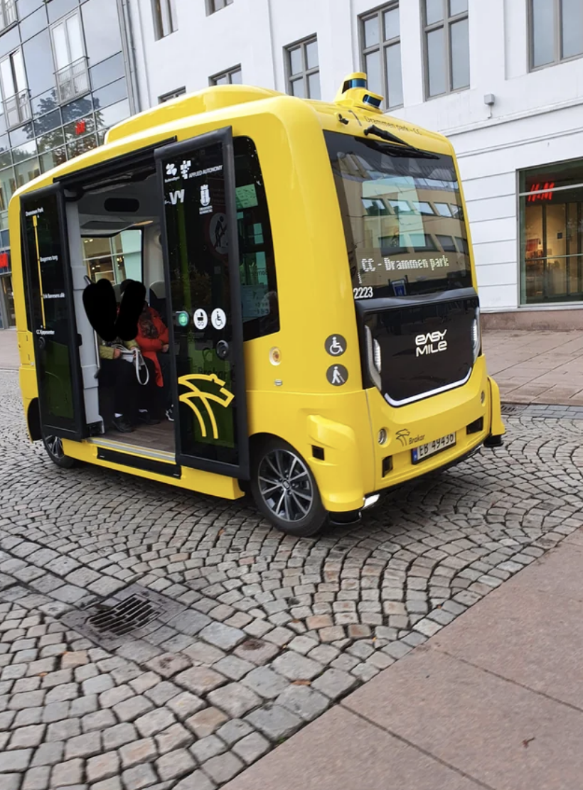 Autonomous yellow shuttle with open door on cobblestone street; no people visible