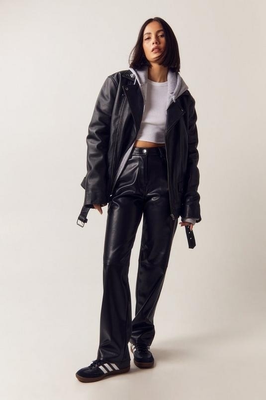 Woman in oversized leather jacket, crop top, and matching pants, standing with hands in pockets