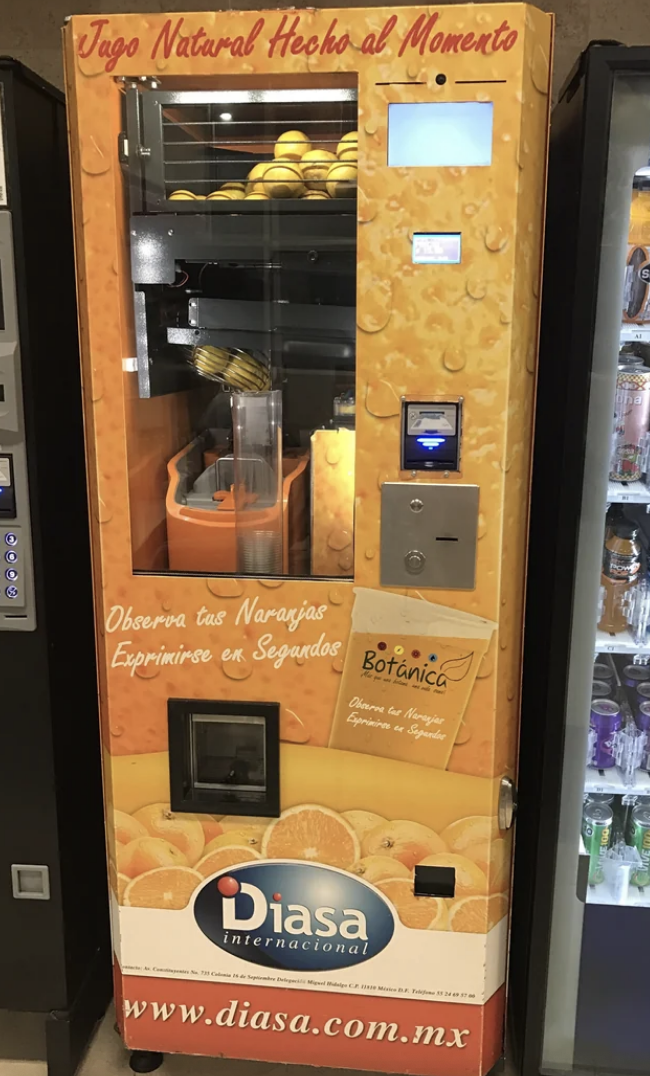 An orange juice vending machine with fresh oranges and a juicing mechanism