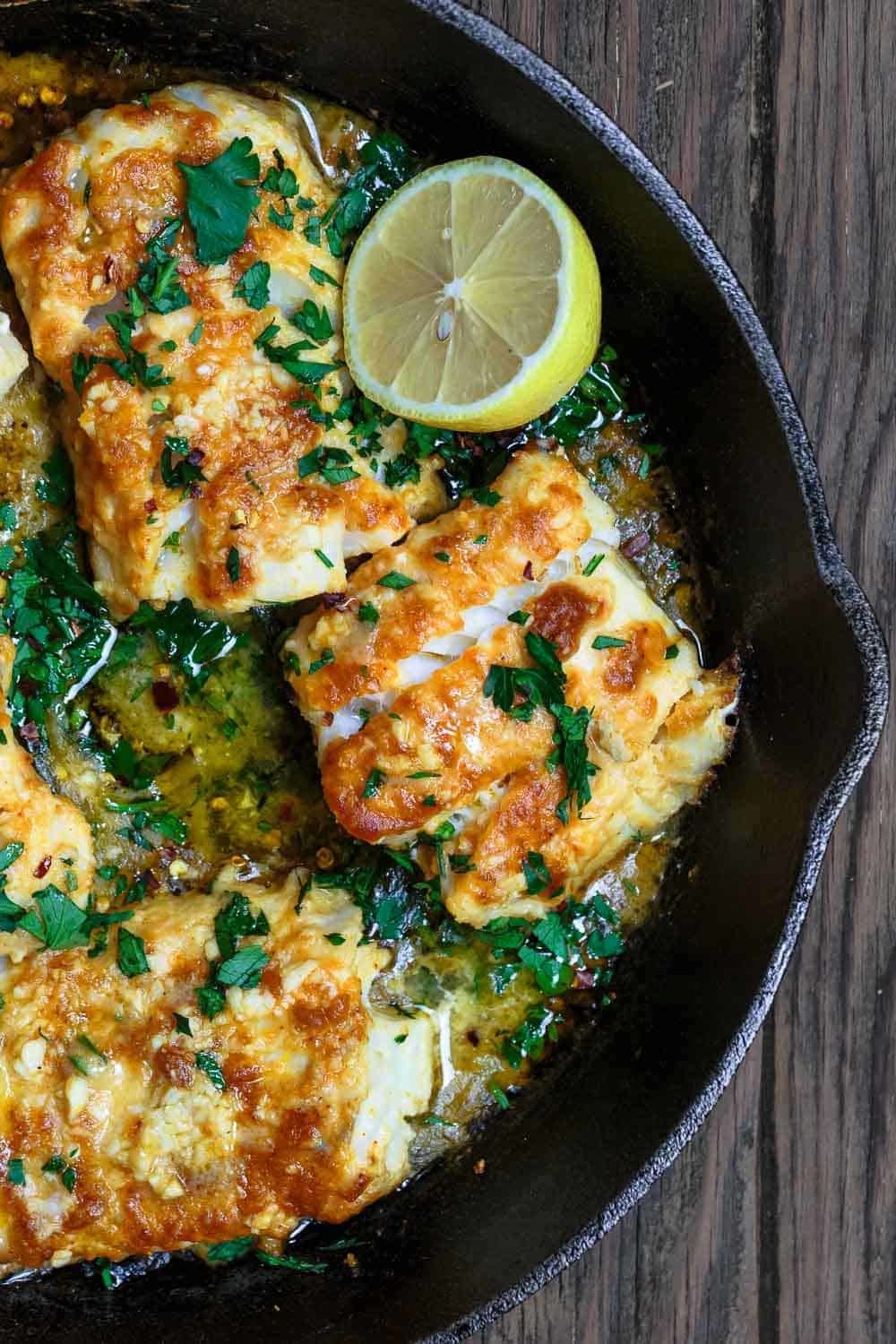 Skillet with cooked chicken, garnished with herbs and lemon slice