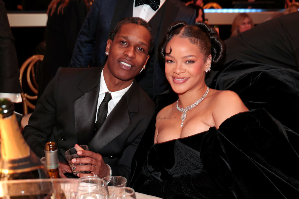 Rihanna and A$AP Rocky seated together at an event, she is wearing a black outfit with a diamond necklace