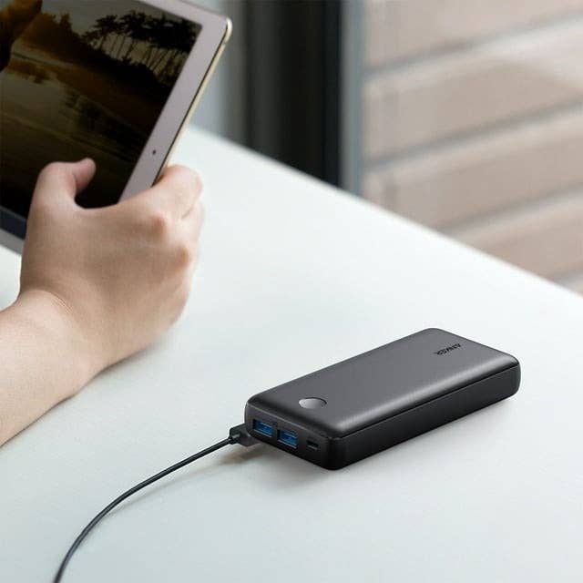 Person holding a tablet connected to a portable battery charger on a table for convenient charging