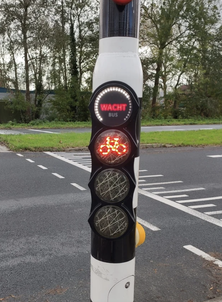 Traffic light for buses displaying a red light with &quot;WACHT&quot; sign illuminated, indicating wait, next to a road