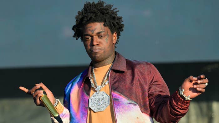 Kodak Black in a shiny jacket and chains performs onstage with a mic in hand
