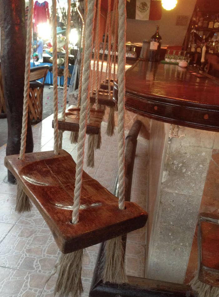 Swing bar stools with ropes suspended from the ceiling in a rustic-themed bar