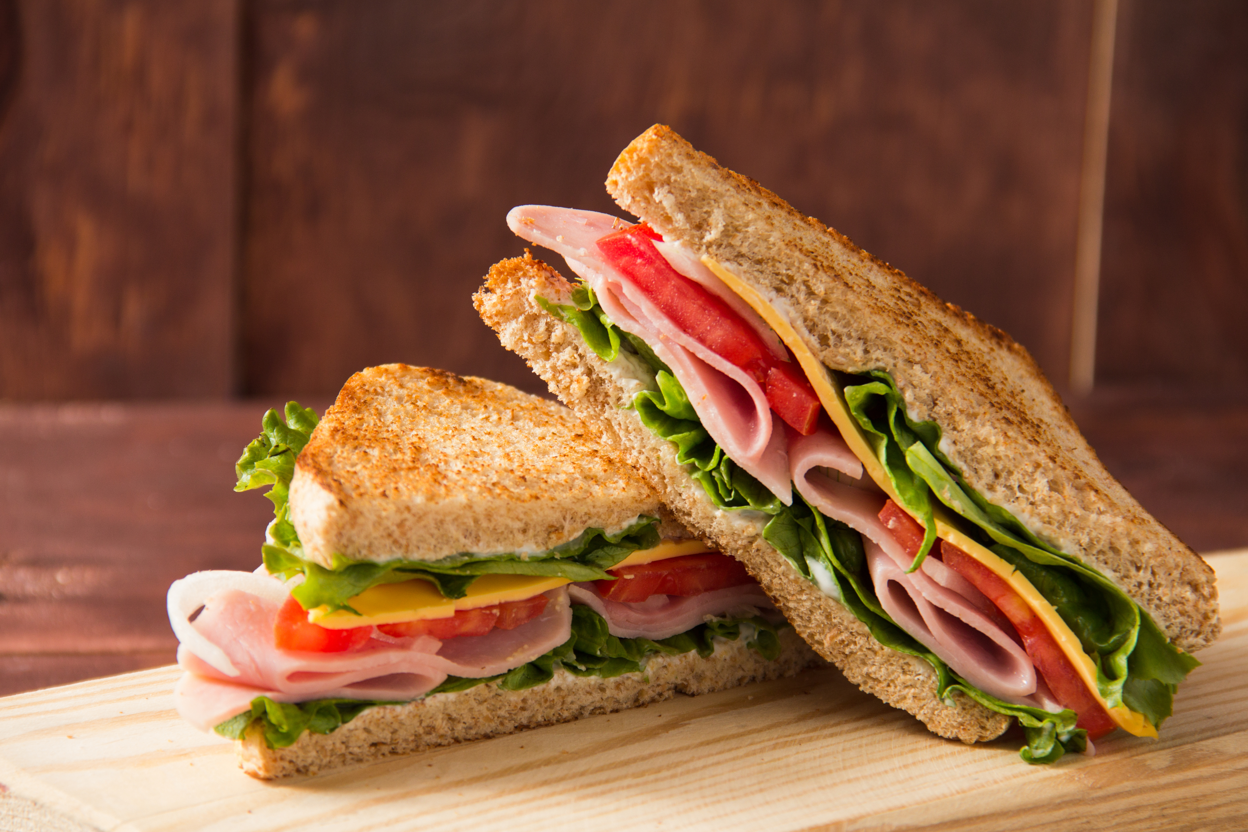 Ham and cheese sandwich with lettuce, tomato, and onions on a wooden surface