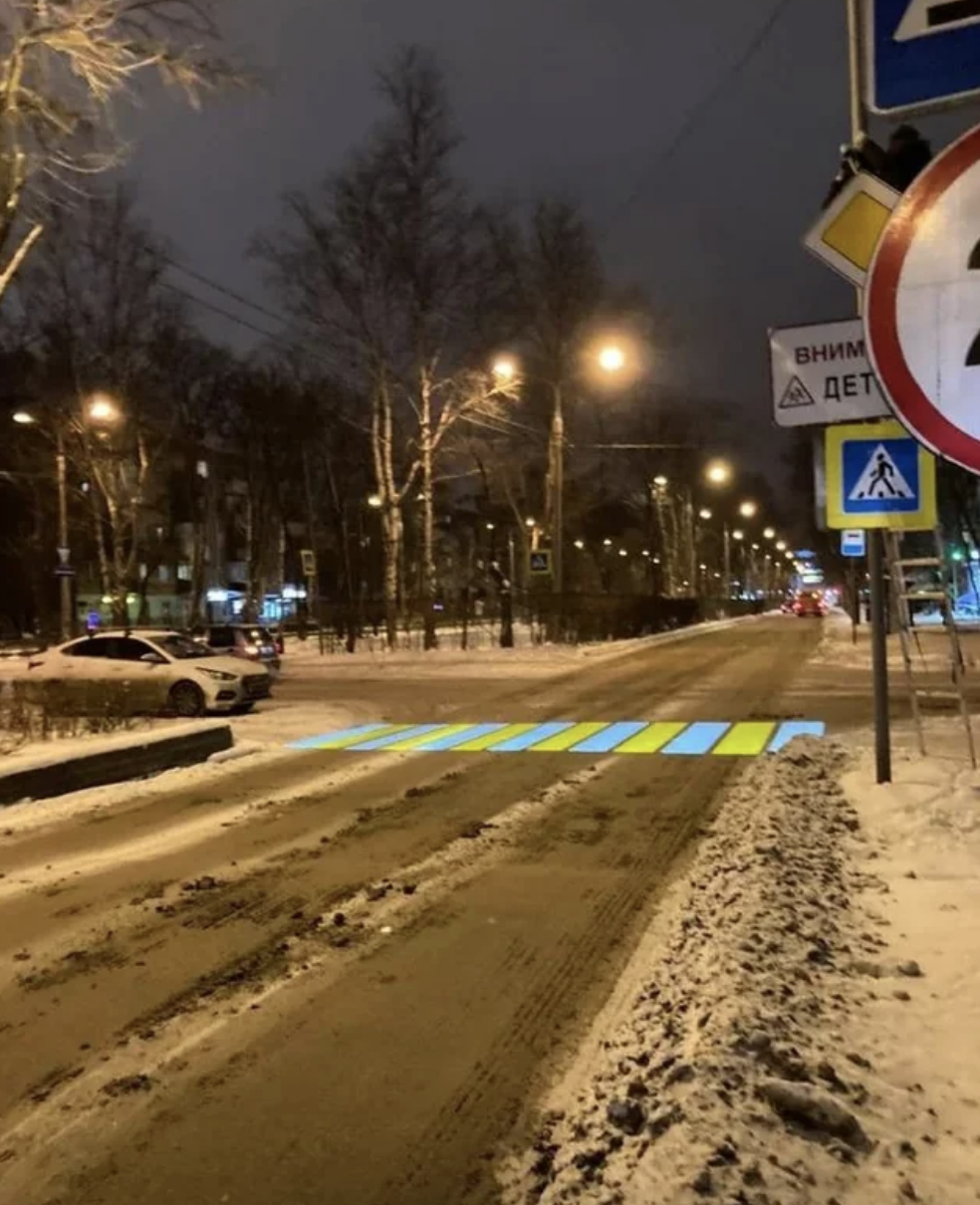 A snowy street at night with a pedestrian crossing and warning signs