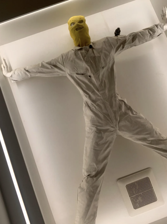 Figure in white protective suit and mask pressed against a translucent surface from below