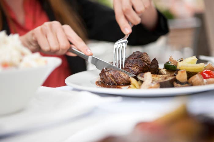 Person dining, cutting into a steak on a plate with roasted vegetables
