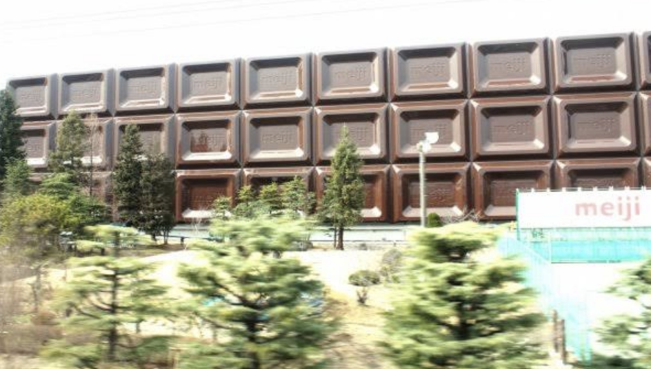 Building facade resembling a bar of chocolate, with &quot;meiji&quot; sign in front