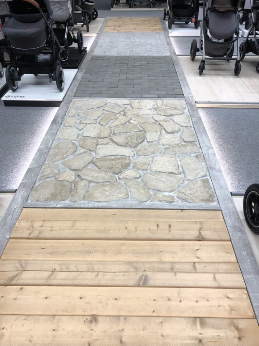 A variety of strollers on either side of a showroom aisle with different floor textures, including wood and stone, for testing