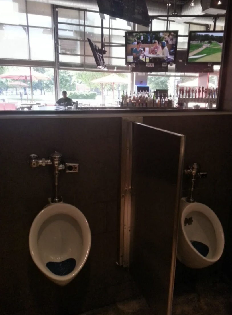 Interior of a men&#x27;s restroom with urinals and televisions mounted above