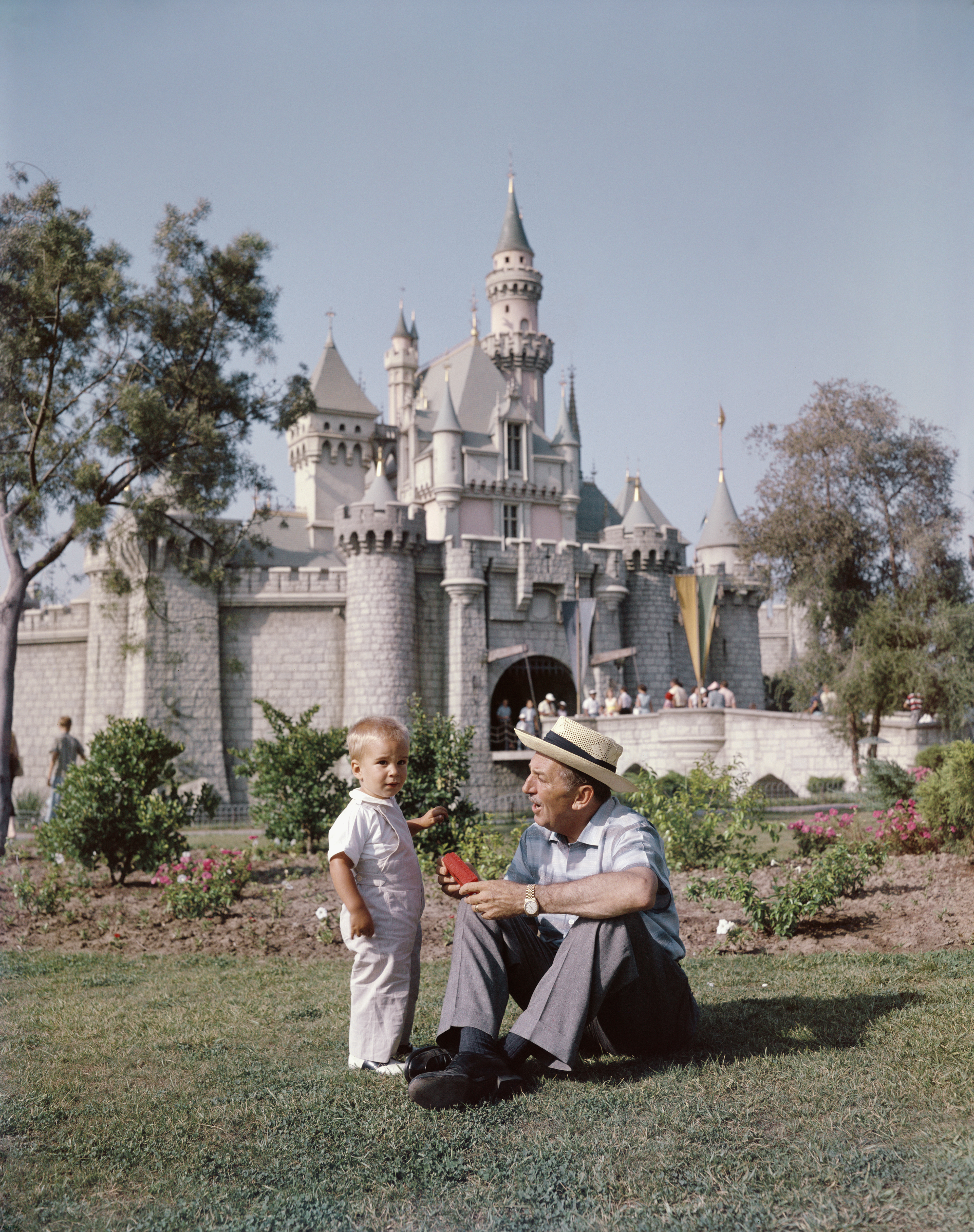 Walt Disney sitting with a young boy in front of Disneyland&#x27;s Sleeping Beauty Castle