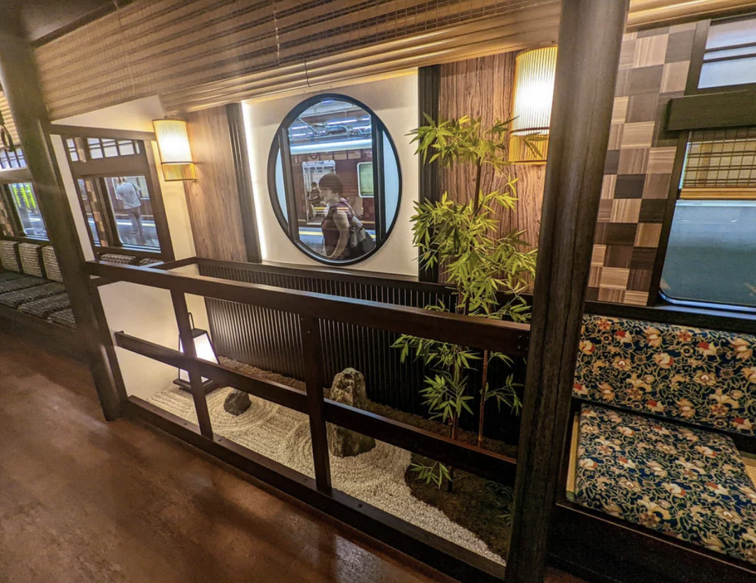 Person reflected in a mirror within a traditionally styled room with decorative plants and seating