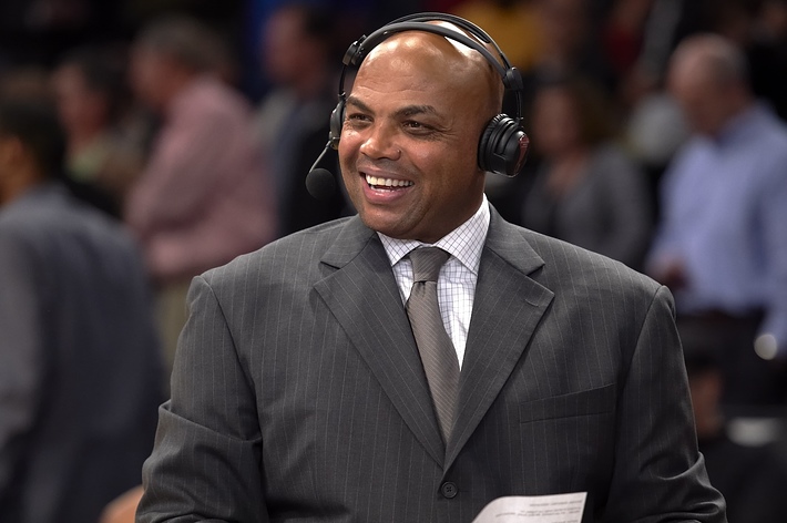 Smiling man in suit with headphones commentating at a sports event