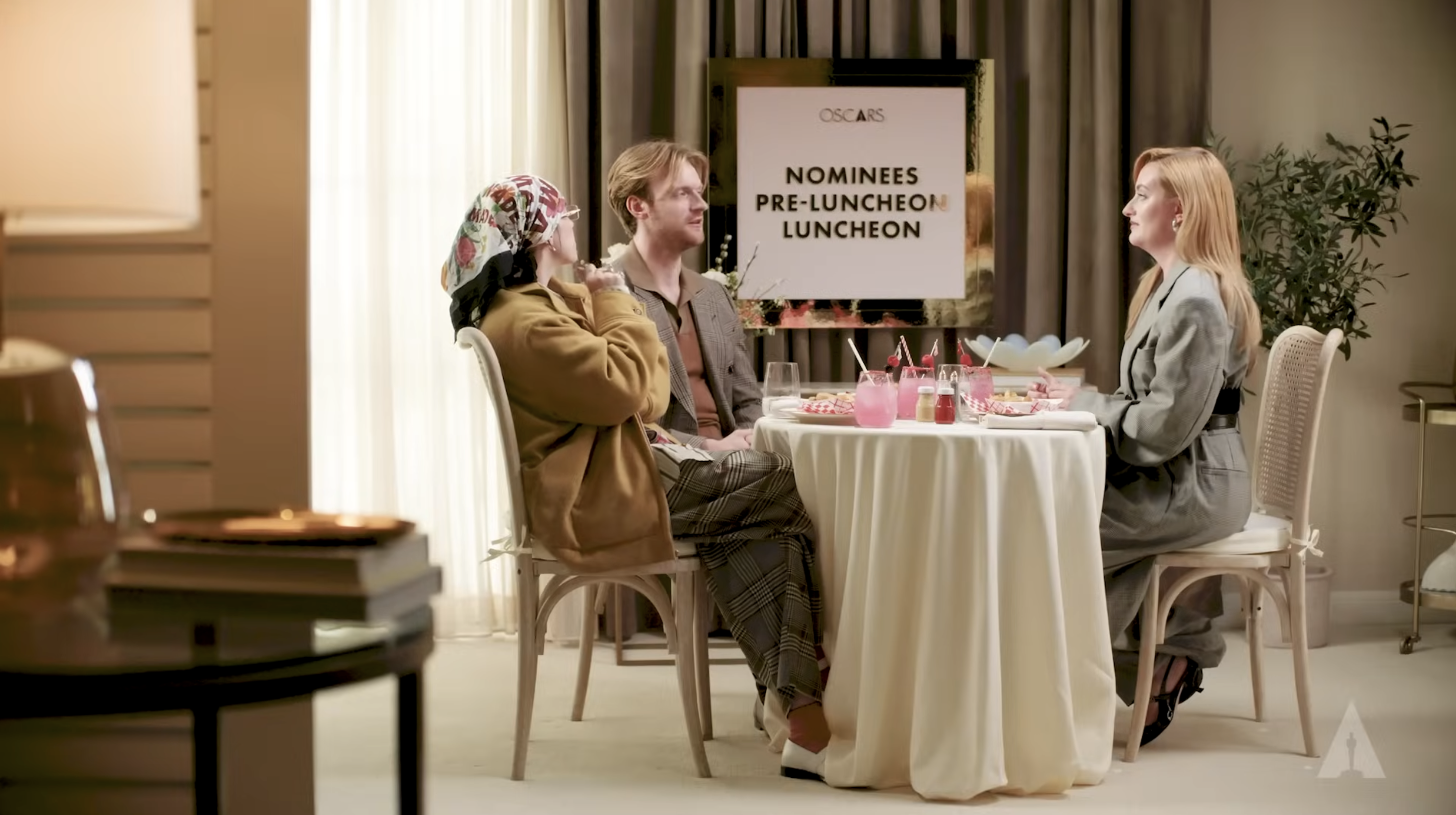The three seated at a table with drinks and decor, including a sign that reads &quot;Oscars Nominees Pre-Luncheon&quot;