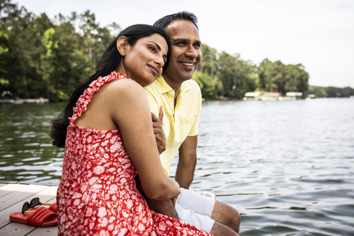 Couple sitting closely on a dock by the lake, smiling and enjoying each other&#x27;s company