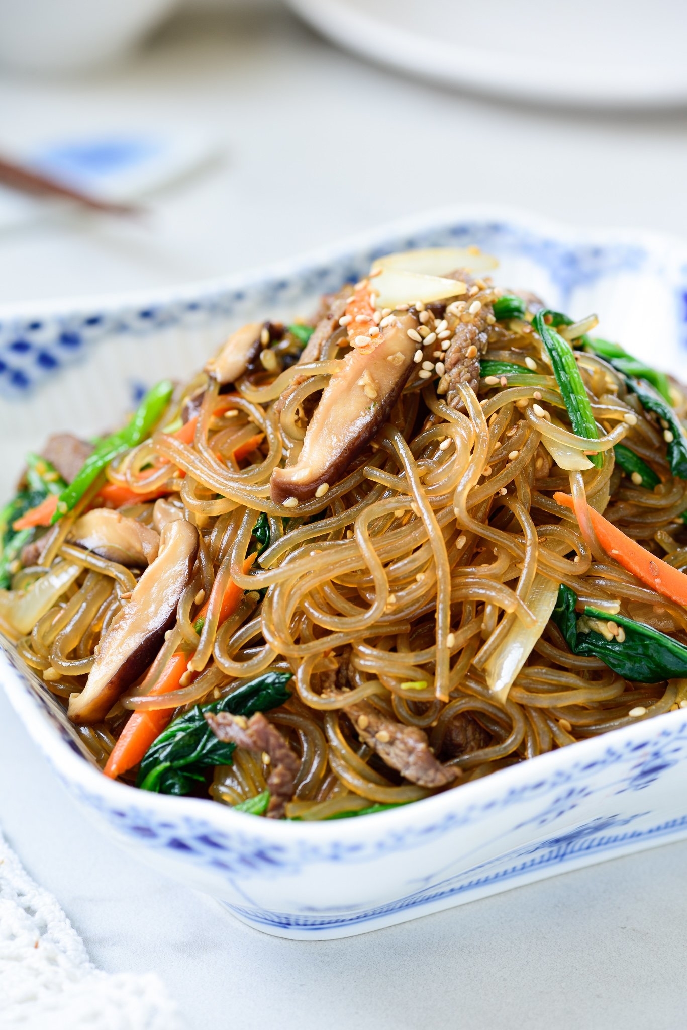 Bowl of stir-fried glass noodles with vegetables and meat, garnished with sesame seeds