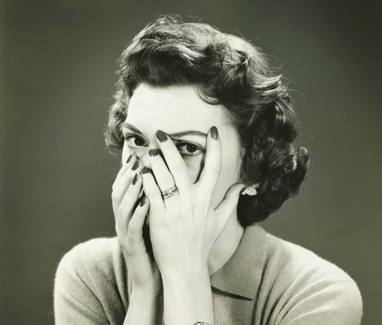 Woman with hands covering face, peeking through fingers, appears pensive or playful