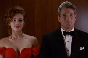 Woman in red off-the-shoulder gown and man in black tuxedo; both smiling. (Characters from a film)