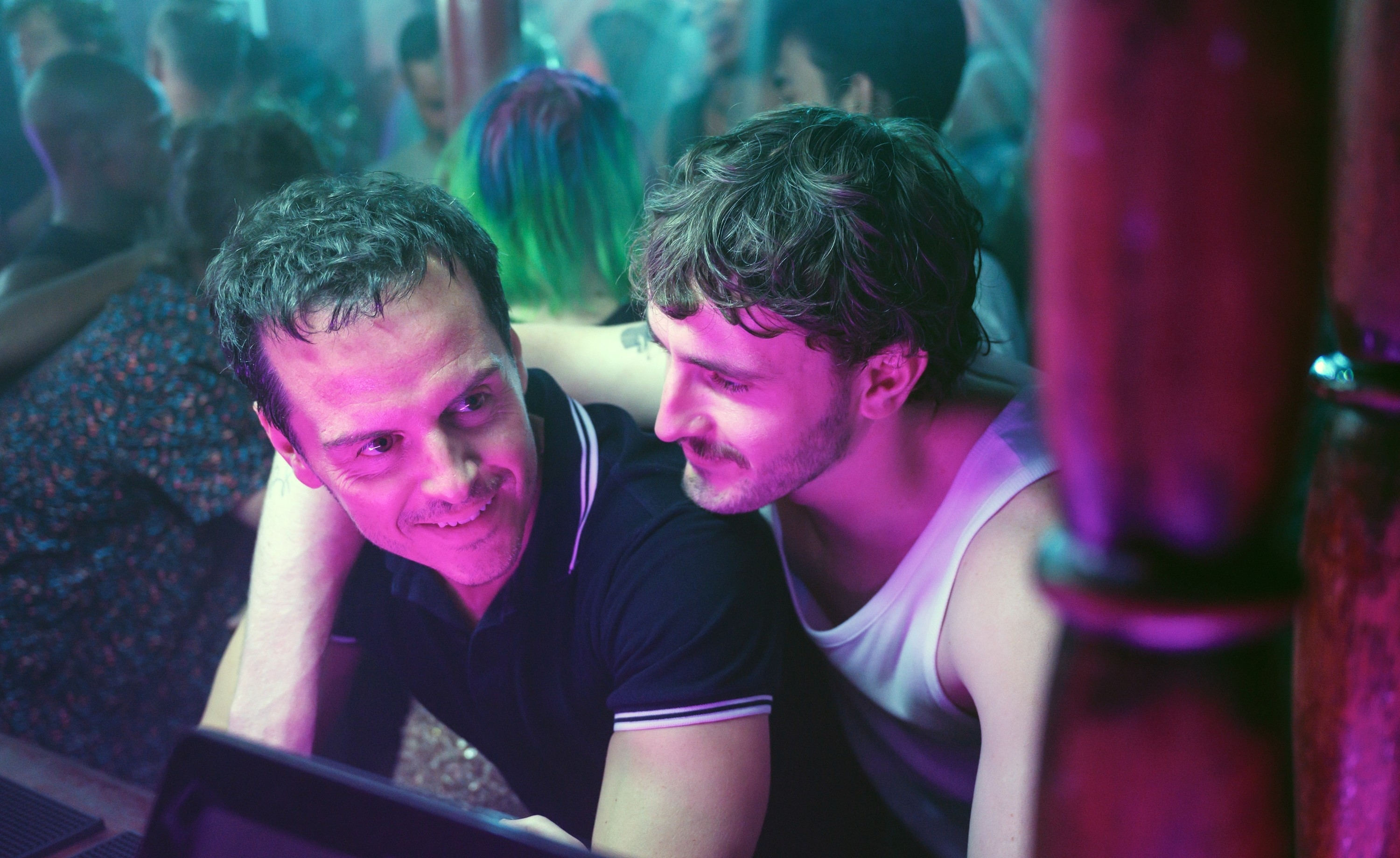 Andrew Scott and Paul Mescal leaning close, sharing a moment in a crowded setting