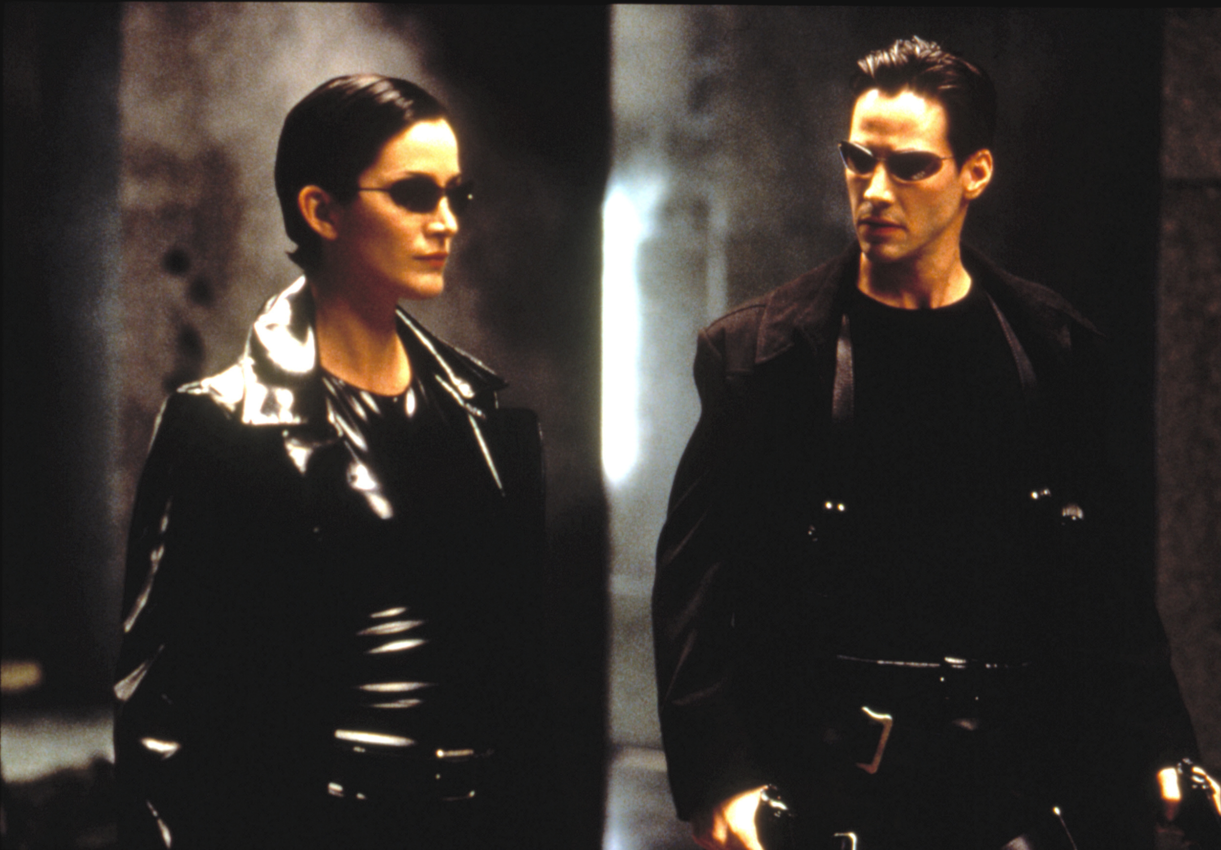 Two characters from The Matrix, Trinity and Neo, stand side by side in black, fitted clothing