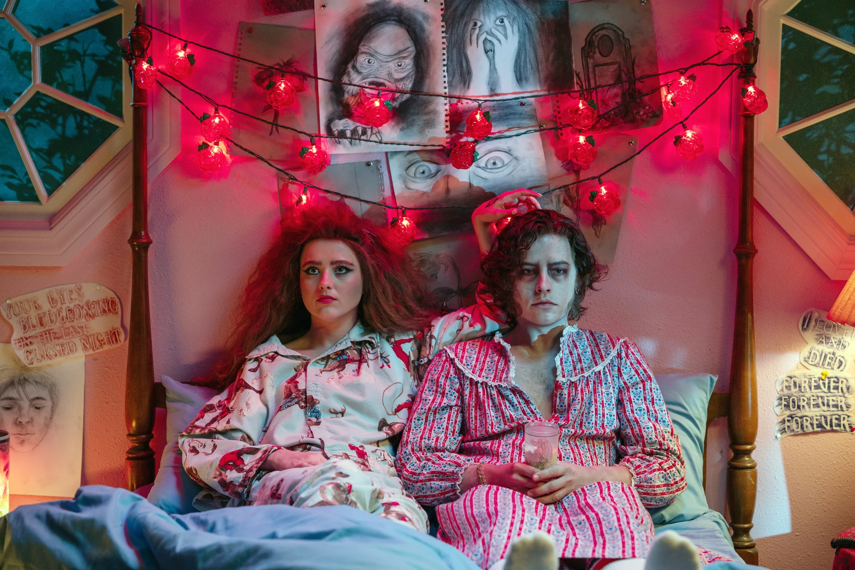 Cole Sprouse and Kathryn Newton in pajamas sit in bed with eclectic decor and string lights