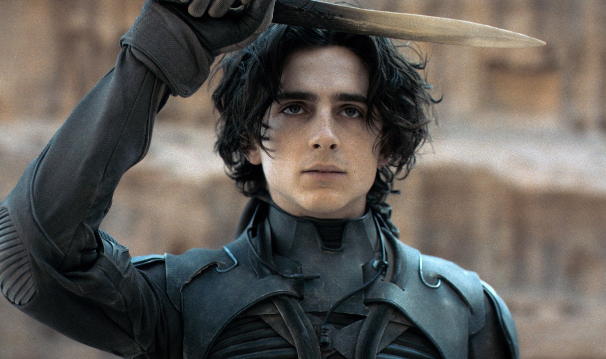 Timothée Chalamet as Paul Atreides in &quot;Dune,&quot; wearing a black stillsuit and holding a knife above his head