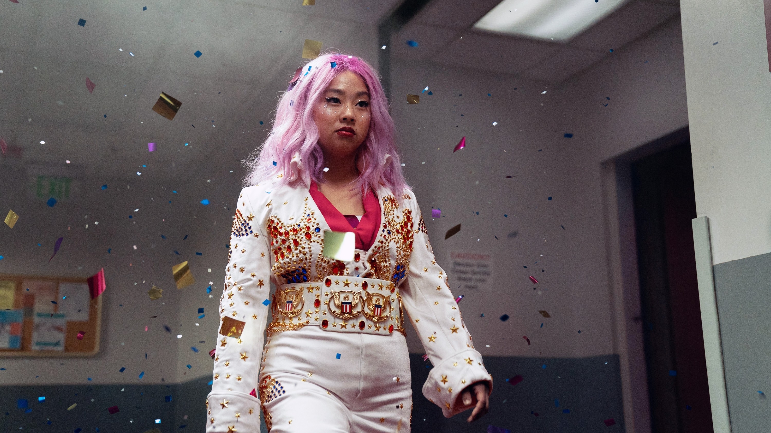 Stephanie Hsu in a bedazzled white suit with a pink undertone walking amid falling confetti