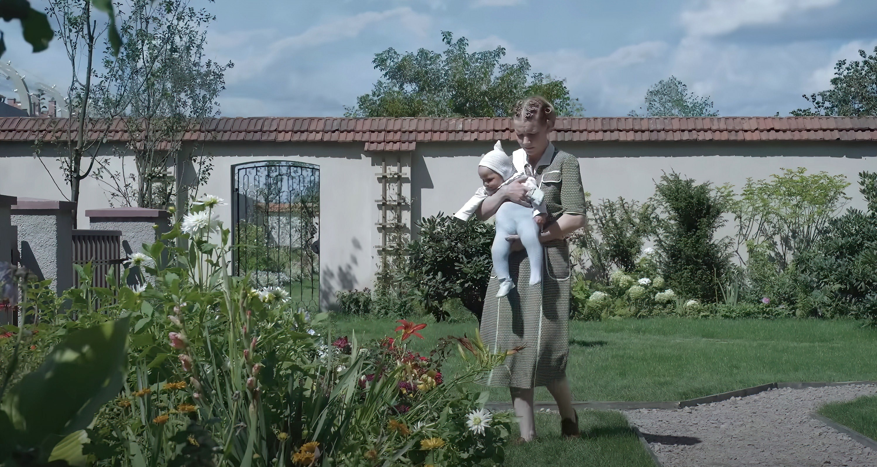 Sandra Hüller holding a baby while walking in a garden