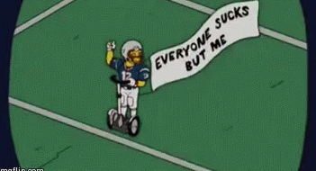 Homer Simpson in a football outfit and helmet, riding a lawn mower, holding a banner