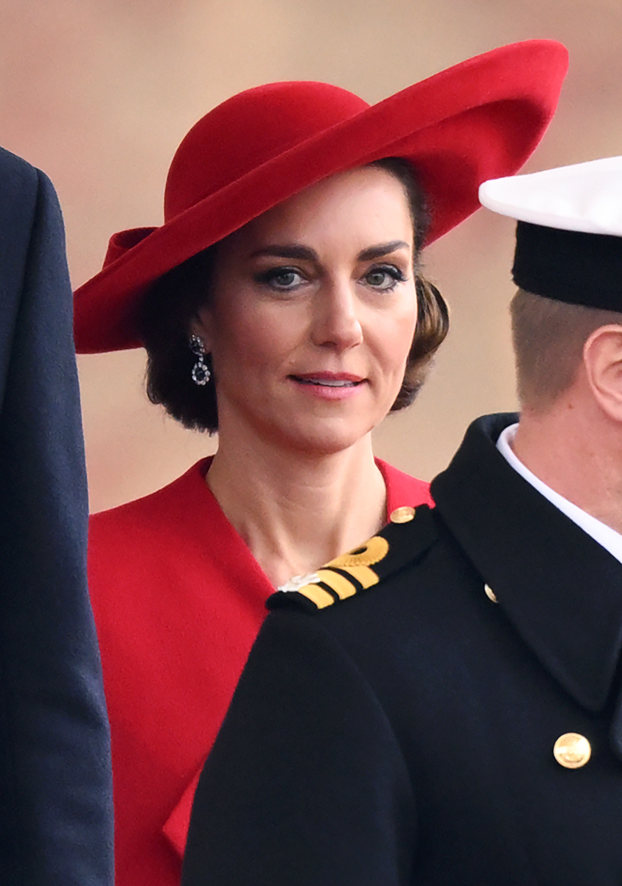 Kate in a red dress and matching hat, with drop earrings, at a formal event