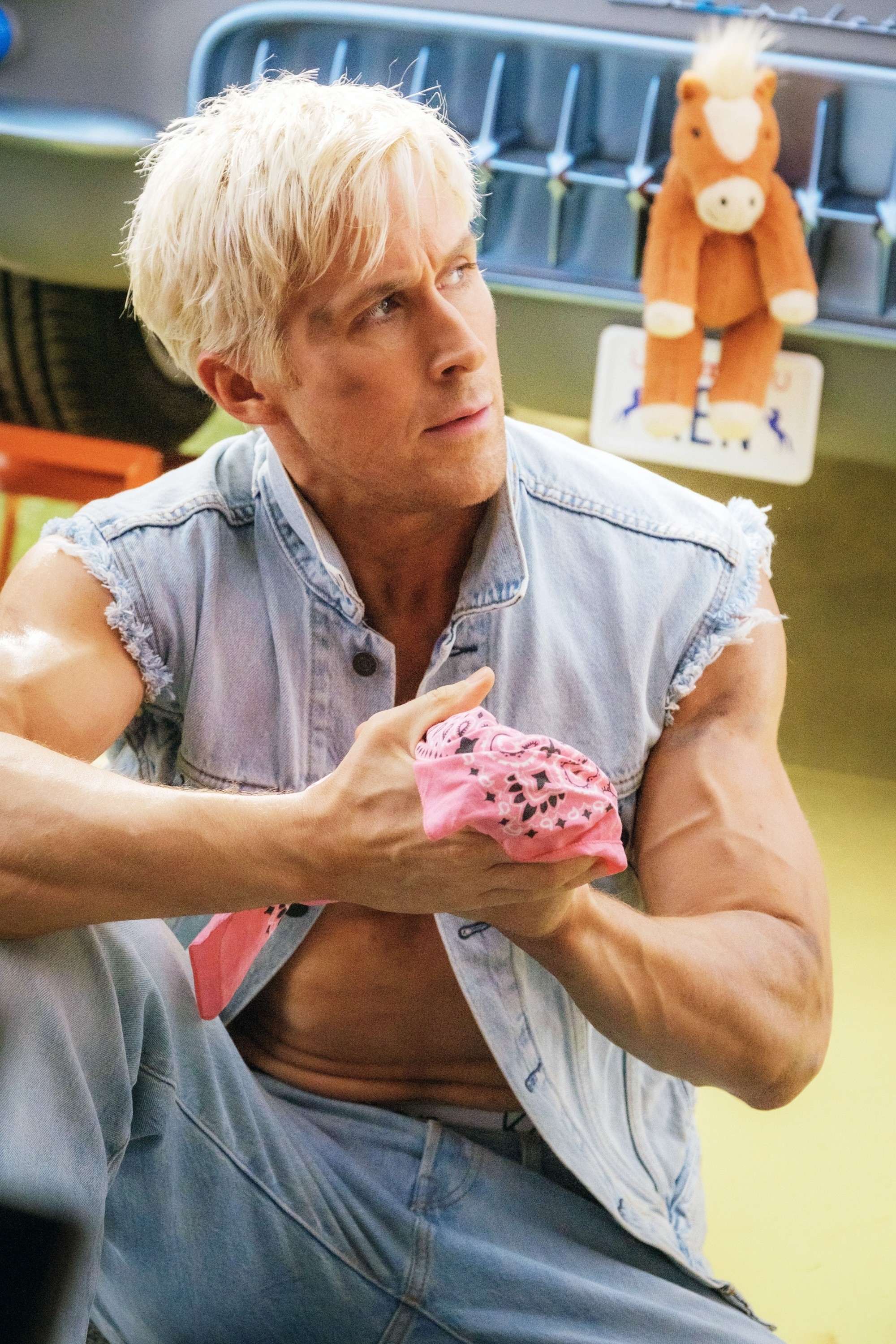 Ryan Gosling in character, wearing a denim vest, posing with an intense look, holding a pink object