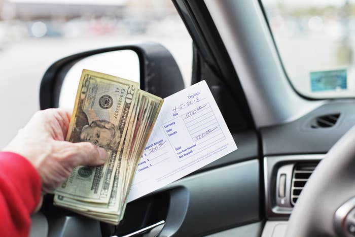 Person holding cash and a check inside a car, likely depicting a financial transaction