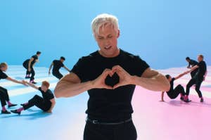 Man in black making a heart shape with hands, dancers in background
