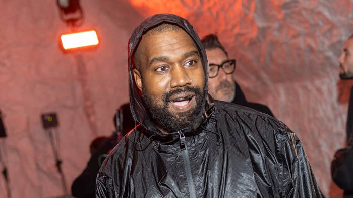 Music artist in hooded jacket at an event, expression focused, others in background