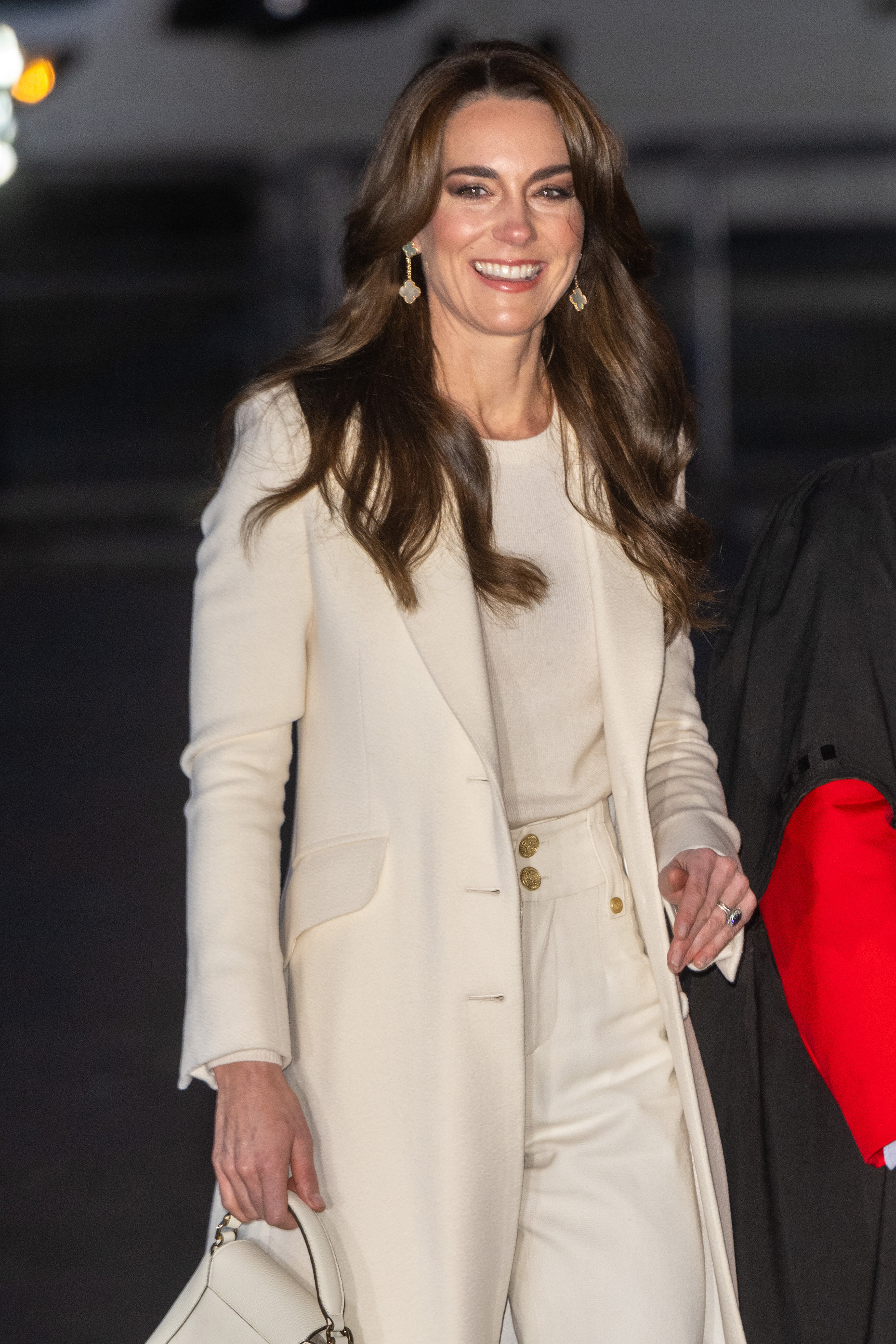 Kate Middleton smiling in an elegant white coat and holding a clutch