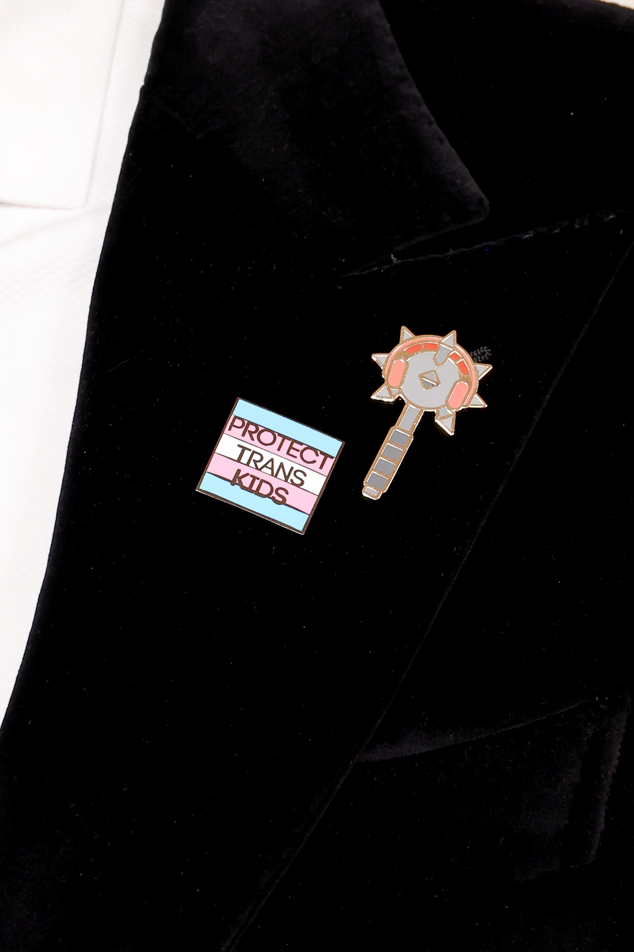 Two lapel pins on a jacket, one with text &quot;PROTECT TRANS KIDS,&quot; and the other shaped like a key