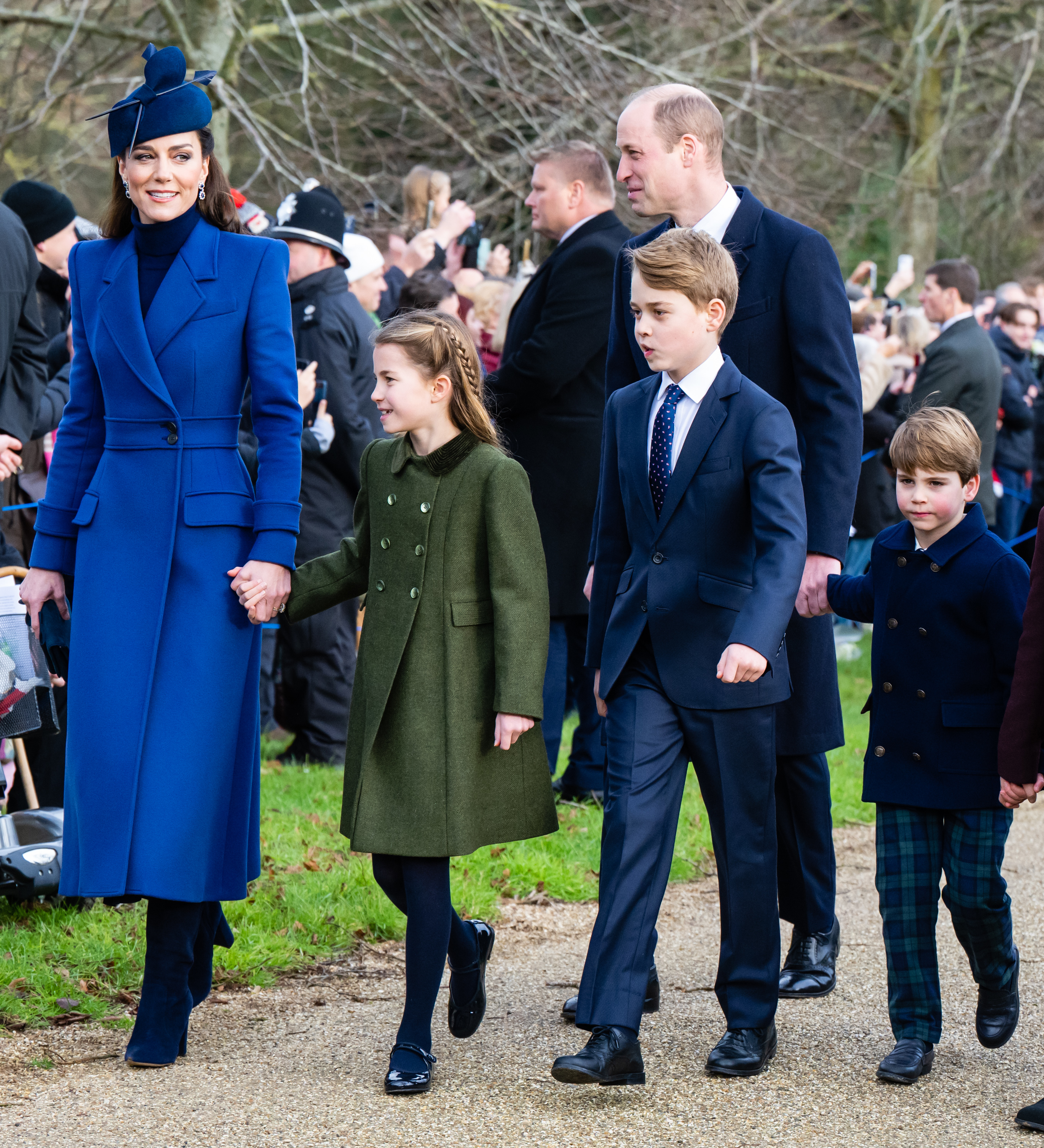 Kate Middleton in a blue coat and hat, walking with Prince William and their three children, all dressed in formal attire