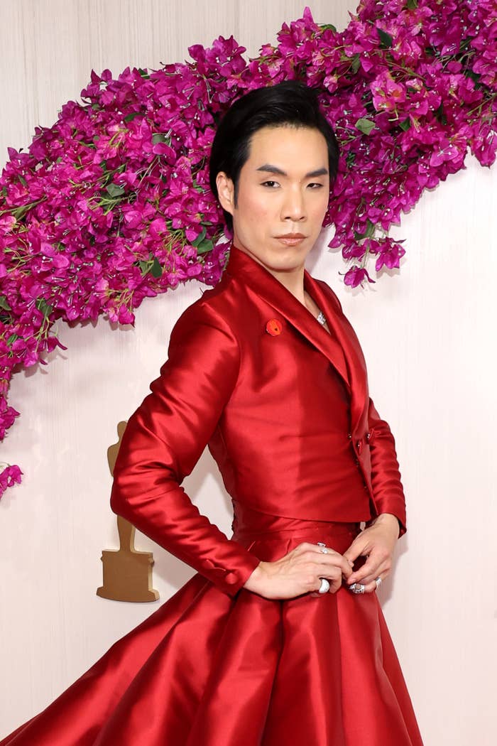 Eugene Lee Yang posing in a red satin suit jacket with an asymmetrical peplum detail