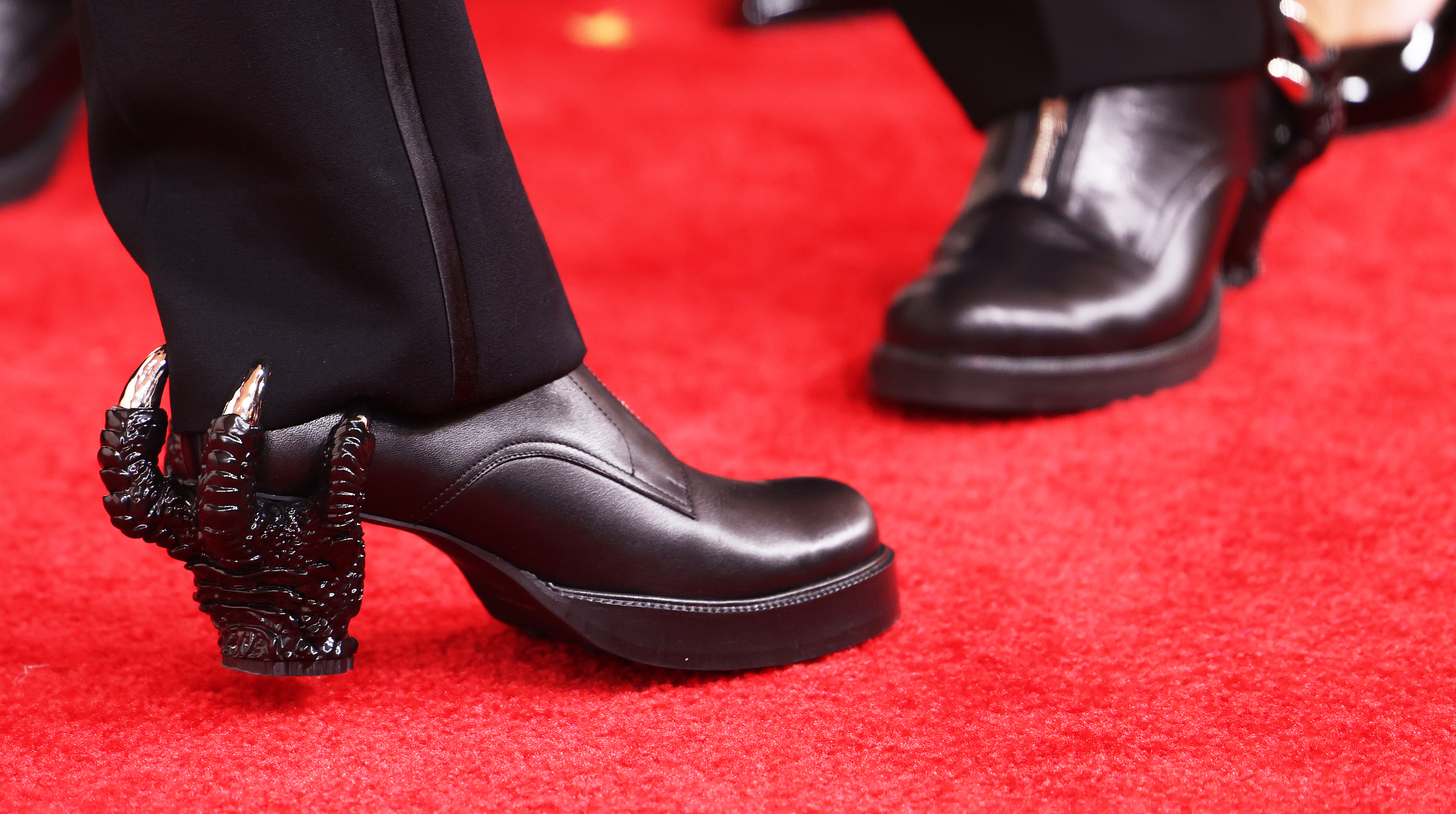 Close-up of a celebrity&#x27;s black shoe with unique claw heel design on the red carpet